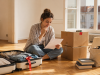 Young woman preparing to move abroad with a suitcase, moving boxes and belongings selected for donation